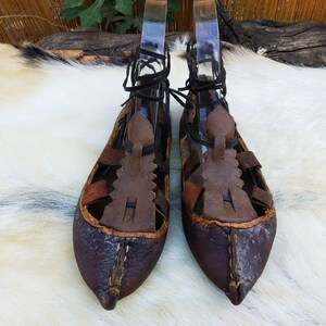 May include: A pair of brown leather sandals with intricate lacing and a pointed toe. The sandals are worn and have a rustic appearance.