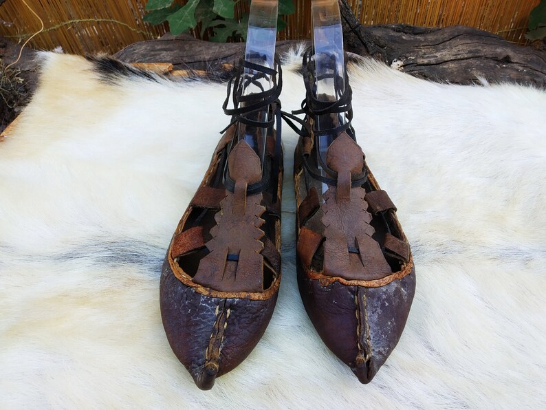 May include: A pair of brown leather sandals with intricate lacing and a pointed toe. The sandals are worn and have a rustic appearance.