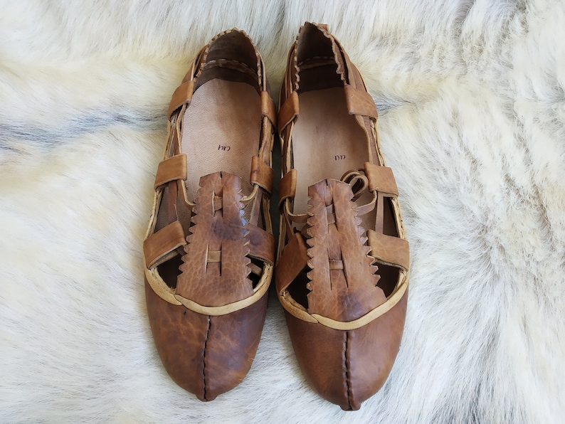 May include: A pair of brown leather sandals with cutouts and a criss-cross strap design. The sandals have a pointed toe and a flat sole.