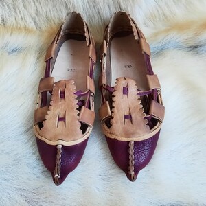 May include: A pair of brown and burgundy leather sandals with a woven design. The sandals have a pointed toe and a size tag that reads "34.5".