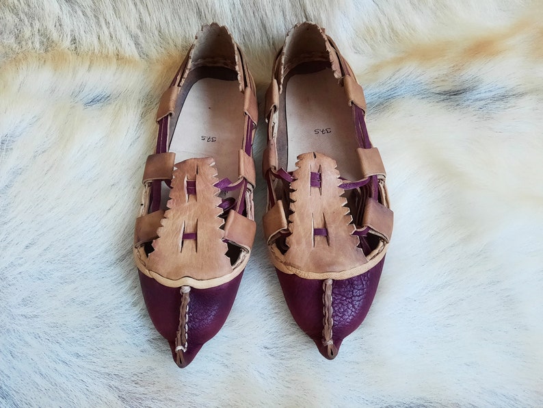 May include: A pair of brown and burgundy leather sandals with a woven design. The sandals have a pointed toe and a size tag that reads "34.5".