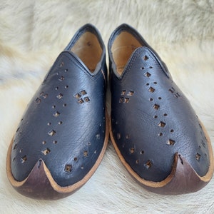 K&ouml;nnte beinhalten: Ein Paar schwarze Slipper aus Leder mit einem dekorativen Muster aus kleinen L&ouml;chern und Diamanten. Die Schuhe haben einen braunen Lederbesatz an den R&auml;ndern.