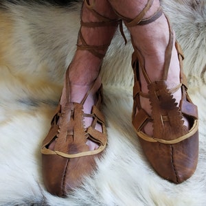 May include: A pair of brown leather sandals with a criss-cross strap design. The sandals have a pointed toe and are tied at the ankle.