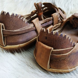 May include: A pair of brown leather sandals with a woven design. The sandals have a thick sole and a strap that goes around the ankle.
