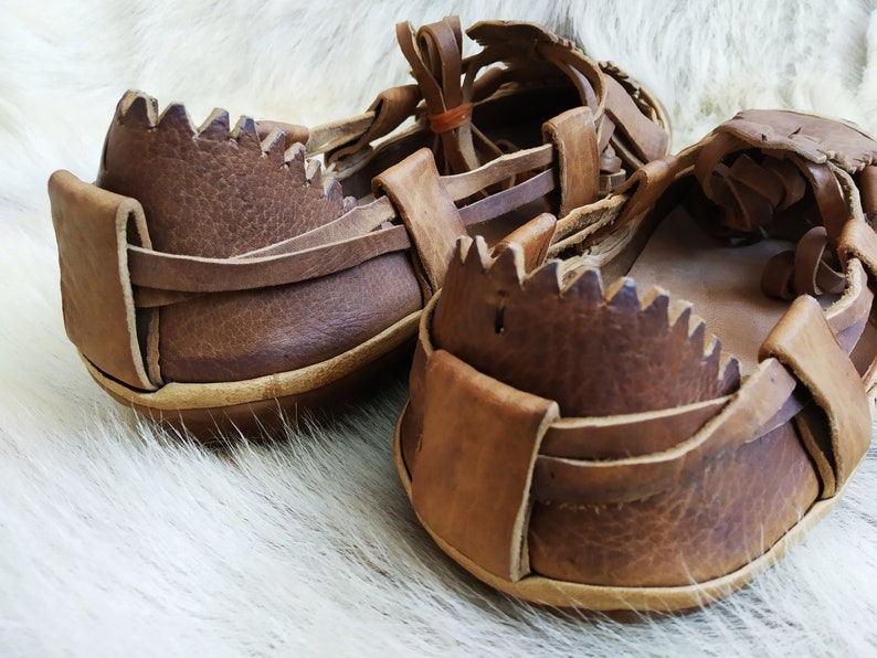 May include: A pair of brown leather sandals with a woven design. The sandals have a thick sole and a strap that goes around the ankle.