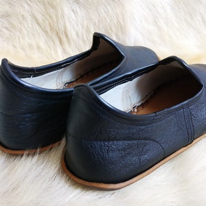 May include: Pair of black leather slip-on shoes with a brown leather sole. The shoes have a simple design and are made of a soft, supple leather.
