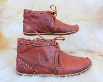 May include: A pair of brown leather ankle boots with laces. The boots have a pointed toe and a decorative stitch pattern around the ankle.