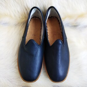 May include: A pair of dark blue leather slippers with a brown leather sole. The slippers have a simple design and are perfect for lounging around the house.