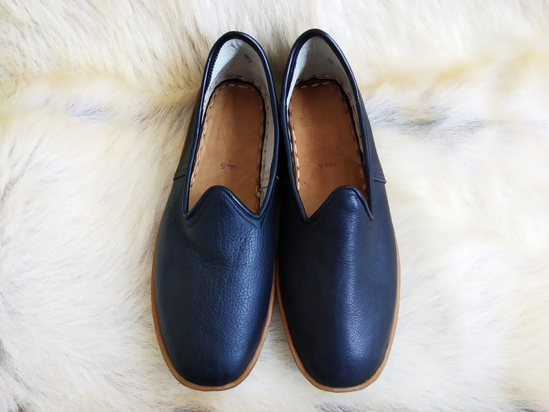 May include: A pair of dark blue leather slippers with a brown leather sole. The slippers have a simple design and are perfect for lounging around the house.