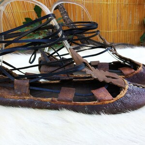 May include: A pair of brown leather sandals with black leather laces. The sandals are tied up the legs and have a pointed toe.