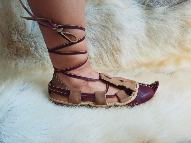 May include: A pair of brown leather sandals with burgundy straps and laces. The sandals have a pointed toe and are tied up the ankle.