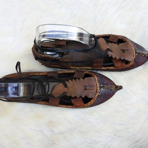 May include: A pair of brown leather sandals with intricate stitching and cutouts. The sandals have laces that tie around the ankle.