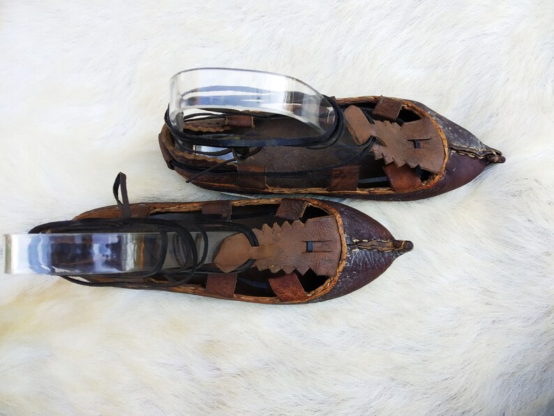 May include: A pair of brown leather sandals with intricate stitching and cutouts. The sandals have laces that tie around the ankle.
