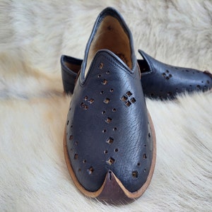 K&ouml;nnte beinhalten: Ein Paar schwarze Lederschuhe mit einem dekorativen Ausschnittmuster. Die Schuhe haben eine spitze Zehenpartie und einen braunen Lederbesatz.