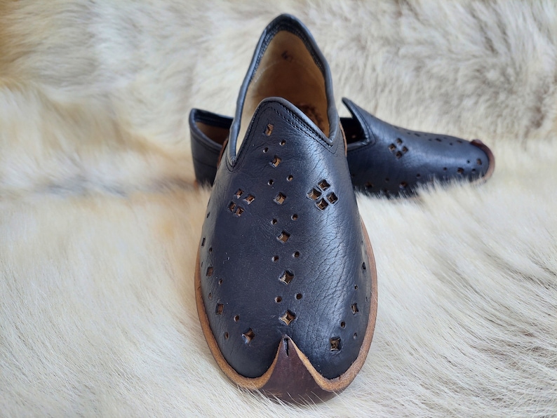 K&ouml;nnte beinhalten: Ein Paar schwarze Lederschuhe mit einem dekorativen Ausschnittmuster. Die Schuhe haben eine spitze Zehenpartie und einen braunen Lederbesatz.