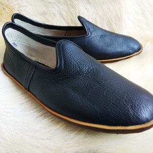 May include: A pair of black leather slip-on shoes with a brown sole. The shoes have a simple design and are made of a soft, supple leather.