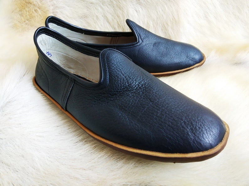 May include: A pair of black leather slip-on shoes with a brown sole. The shoes have a simple design and are made of a soft, supple leather.