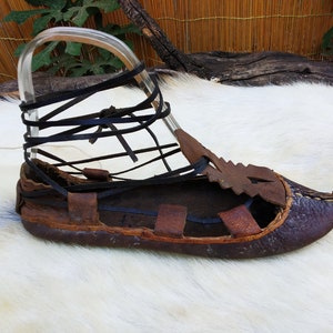 May include: A brown leather sandal with a black leather strap and a white fur background.