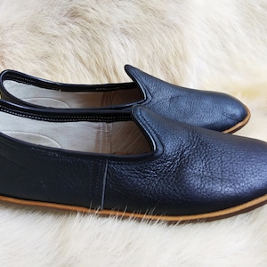 May include: A pair of black leather slip-on shoes with a brown leather trim around the sole.
