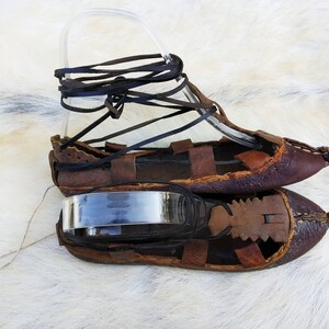 May include: A pair of brown leather sandals with laces. The sandals are tied together with a clear plastic strap.