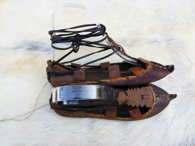 May include: A pair of brown leather sandals with laces. The sandals are tied together with a clear plastic strap.