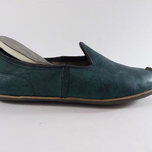 May include: A dark green leather slipper with a brown sole. The slipper has a rounded toe and a simple design.