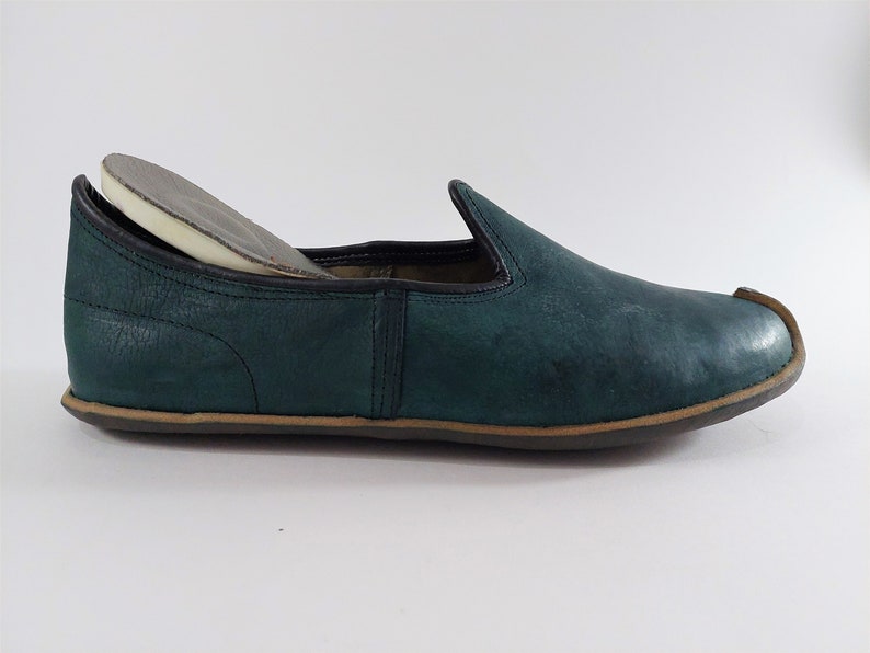 May include: A dark green leather slipper with a brown sole. The slipper has a rounded toe and a simple design.