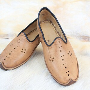 Pu&ograve; includere: Un paio di scarpe da uomo in pelle color cuoio con bordi neri e tagli decorativi. Le scarpe hanno una punta a punta e una suola piatta.
