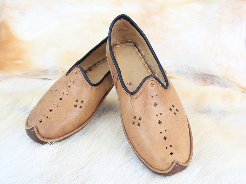 Pu&ograve; includere: Un paio di scarpe da uomo in pelle color cuoio con bordi neri e tagli decorativi. Le scarpe hanno una punta a punta e una suola piatta.