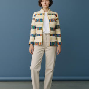 Peut inclure: Une femme porte une veste crème à rayures colorées, un t-shirt blanc et un pantalon beige. La veste a une bordure jaune. Elle porte des baskets blanches.