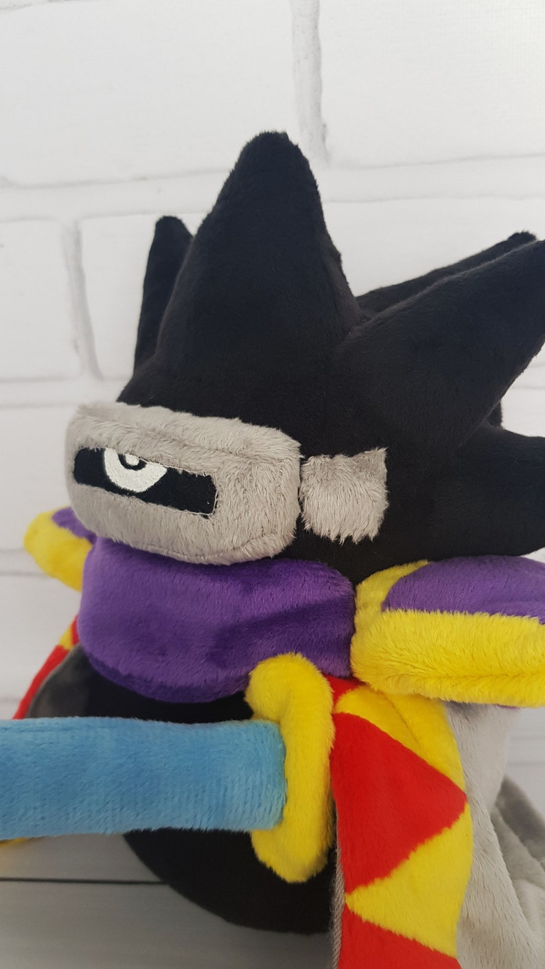 May include: Black, gray, purple, yellow, and red plush toy with a single eye and a sword.