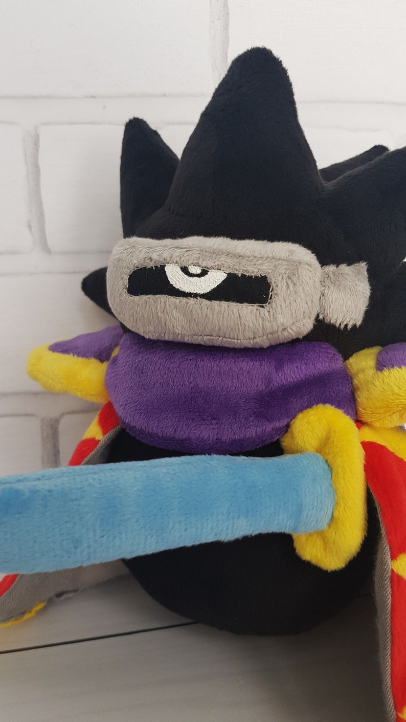 May include: Black plush toy with a purple and yellow cape, a gray mask with a white eye, and a blue sword.