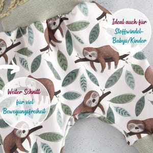 May include: Baby pants featuring a white background with a repeating pattern of brown sloths resting on branches and green leaves. The garment has a wide, ribbed olive green waistband and matching ribbed leg cuffs. A small white brand tag is visible.
