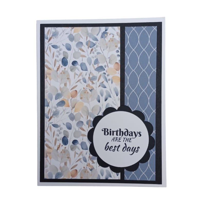 May include: A greeting card with a blue and white floral pattern on the left side and a blue patterned background on the right side. The card has a black scalloped circle with the text "Birthdays are the best days" in white.