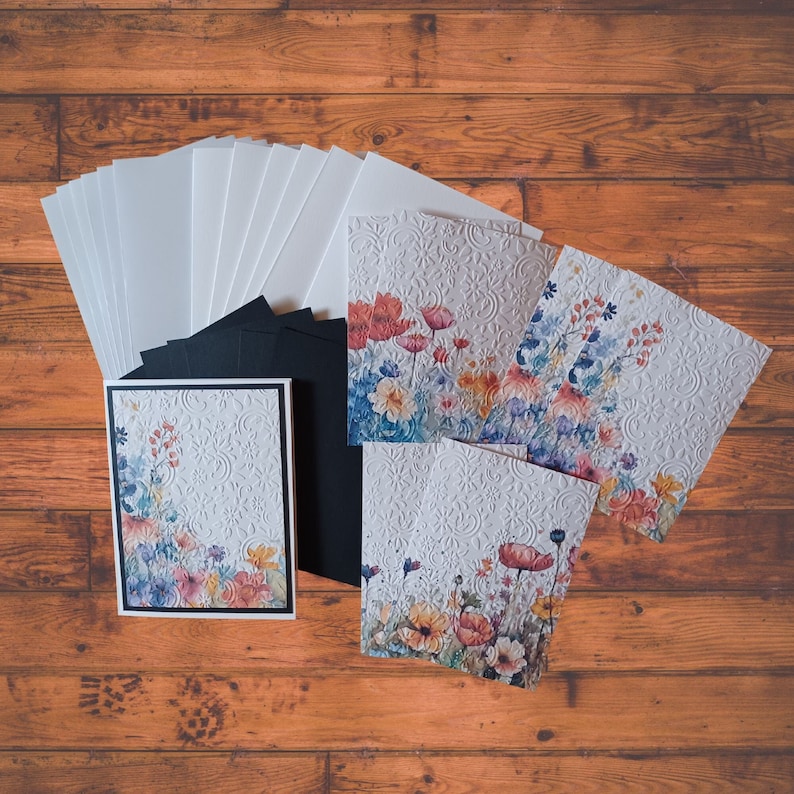 Puede incluir: Un conjunto de tarjetas en blanco con dise&ntilde;os florales. Las tarjetas son blancas con un patr&oacute;n en relieve y presentan ilustraciones florales de acuarela en tonos de rosa, azul y verde.