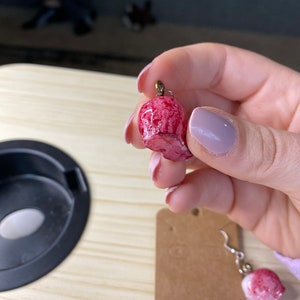 K&ouml;nnte beinhalten: Ein Paar rosa und wei&szlig;e Totenkopf-Ohrringe mit goldenen Haken. Die Ohrringe sind aus Polymer Clay gefertigt und haben einen Marmoreffekt.