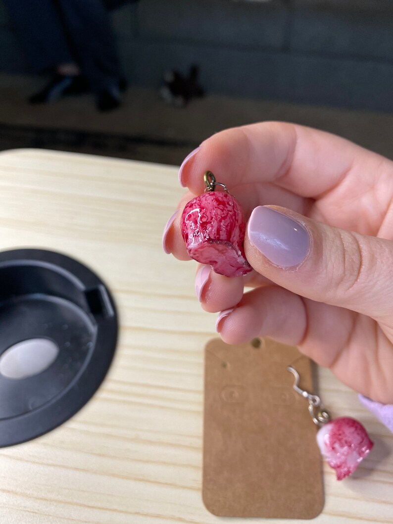 K&ouml;nnte beinhalten: Ein Paar rosa und wei&szlig;e Totenkopf-Ohrringe mit goldenen Haken. Die Ohrringe sind aus Polymer Clay gefertigt und haben einen Marmoreffekt.