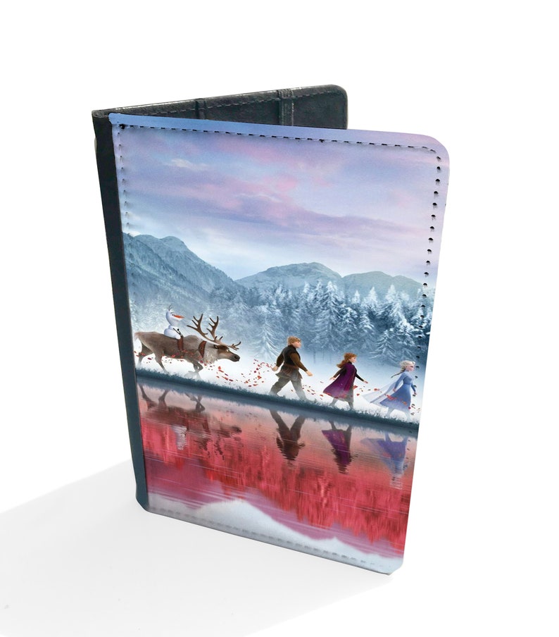 May include: A passport cover featuring a winter scene with a group of people walking through a snowy forest. The characters are from the movie Frozen II. The cover is made of a durable material and has a stitched edge.