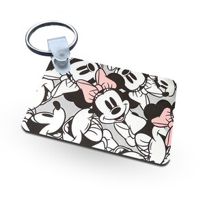 May include: A white and black rectangular keychain with a repeating pattern of Mickey Mouse and Minnie Mouse faces. The keychain has a silver metal ring.
