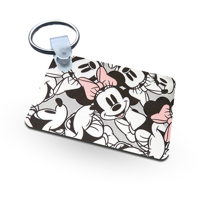 May include: A white and black rectangular keychain with a repeating pattern of Mickey Mouse and Minnie Mouse faces. The keychain has a silver metal ring.