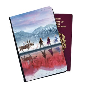 May include: A passport holder featuring a colorful illustration of characters from the movie Frozen walking through a snowy forest with a reindeer. The background is a pink and blue sky with mountains in the distance. The holder has a black border and a stitched edge.