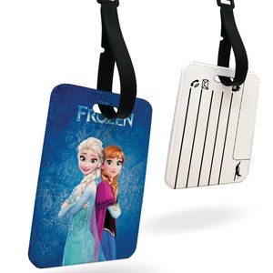 May include: A blue and white luggage tag featuring Elsa and Anna from the film Frozen. The tag has a black strap and a white writing area on the reverse.
