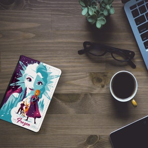 May include: A white and purple phone case with a colorful illustration of Elsa and Anna from the movie Frozen. The case features the text "Frozen" in pink.