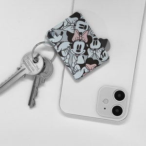 May include: A white smartphone with a black camera lens and a Mickey Mouse and Minnie Mouse character phone grip attached to the back.