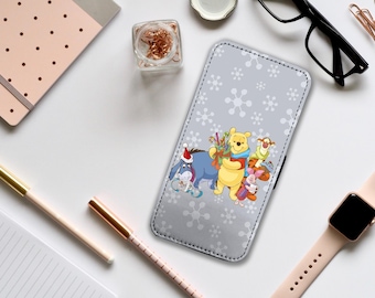 May include: A gray phone case with a white snowflake pattern. The case features a cartoon image of Winnie the Pooh and his friends, including Piglet, Tigger, and Eeyore. The characters are dressed in winter clothing and holding gifts.