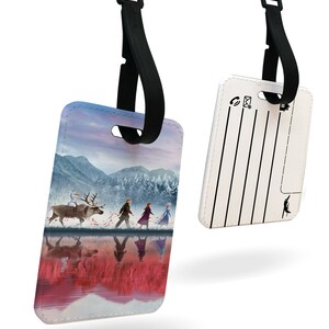 May include: A luggage tag with a colorful image of characters from the movie Frozen II. The tag has a black strap and a white back with lines for writing contact information.