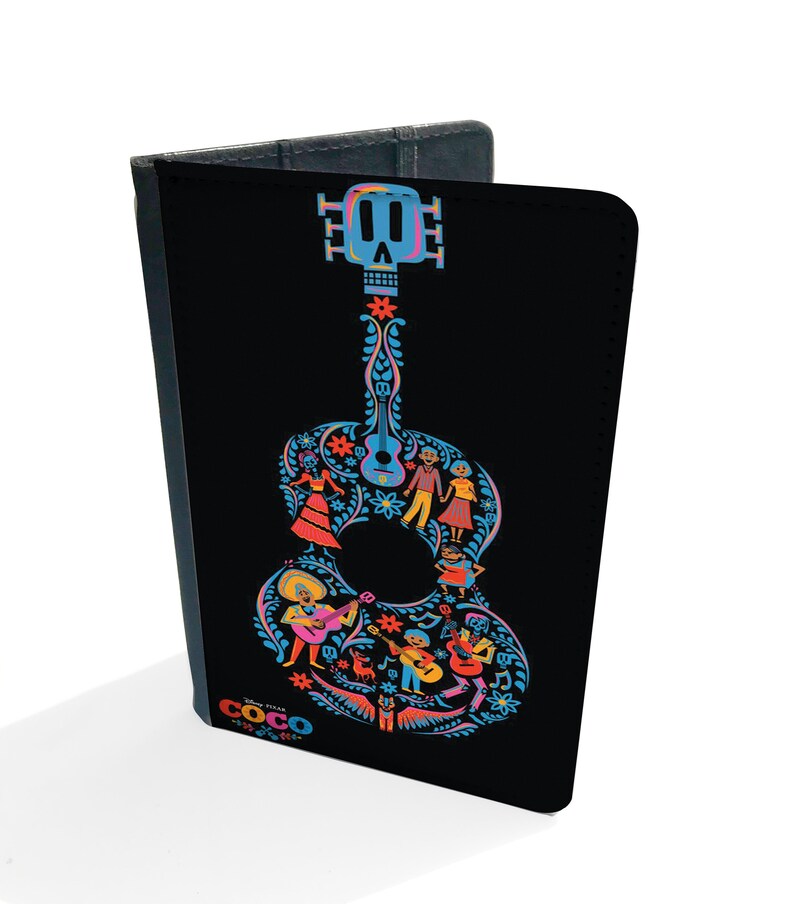 May include: Black passport holder with a colorful guitar design featuring a skull and characters from the Disney Pixar movie Coco. The text "Coco" is printed on the bottom of the holder.