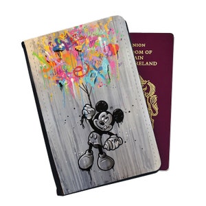 May include: A passport holder with a black background and a colourful graffiti design featuring Mickey Mouse holding onto a bunch of balloons. The design is on a wood-like surface.