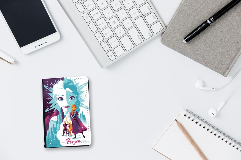 May include: A white and purple passport holder with a Frozen design featuring Elsa and Anna. The design includes a snowflake pattern and the word "Frozen" in pink letters.