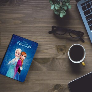 May include: A blue notebook with a Disney Frozen design featuring Elsa and Anna. The notebook has a stitched edge and the title "Disney Frozen" is printed on the cover.